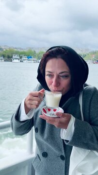 Smiling  woman holding traditional turkish winter drink salep on ferry boat at Golden Horn in Istanbul, Turkey. Hot milky beverage with cinnamon, authentic local lifestyle and Bosphorus.