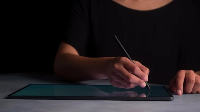 Close-up of hands drawing or writing on a digital tablet with a digital pen in low light conditions