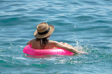 Obraz premium Woman Swimming Sea: Woman in hat relaxing, floating pink tube, splashing warm ocean water on sunny day.