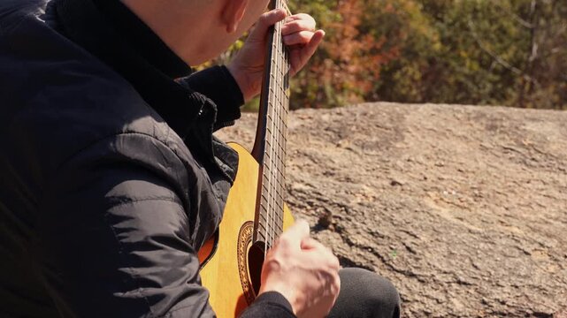 Close up hands of artist plays wooden acoustic guitar in autumnal park. Young songwriter plays string musical instrument hobby outside in nature fall time. Audio music healing in natural surrounding. 