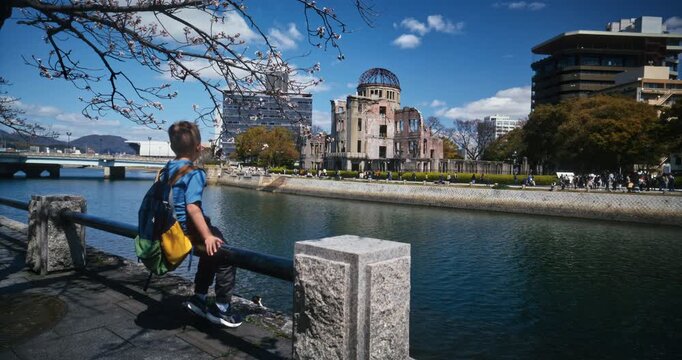 Child Gazing at Atomic Bomb Dome Across River In Hiroshima, Japan - Slow Motion Wide Shot