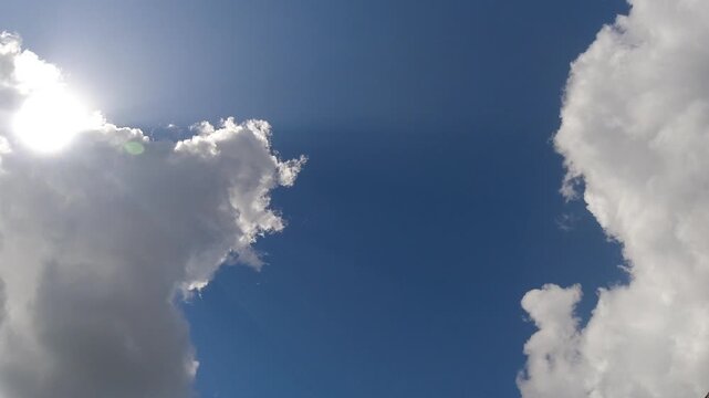 Mesmerizing hyperlapse video of fluffy clouds rolling across a vibrant blue summer sky, revealing bright sunbeams, lens flares, and dynamic weather changes on a beautiful sunny morning.