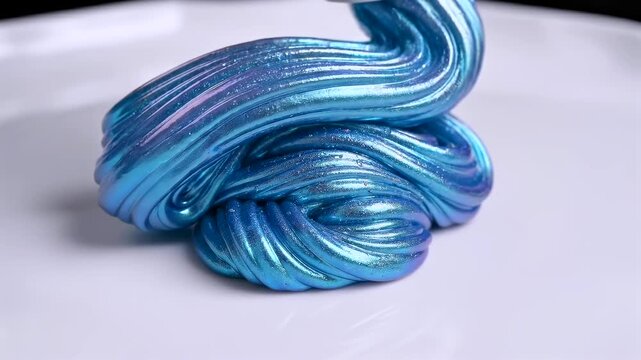 Tight macro of thick blue gel extruding from a nozzle and contacting a smooth porcelain surface. Focus on texture, viscosity, and glossy folds as the product coils and builds a dense layered shape