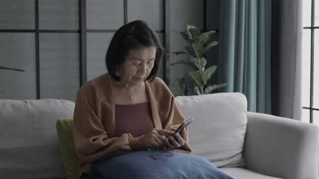 Asian mature woman using credit card booking ticket online on smartphone