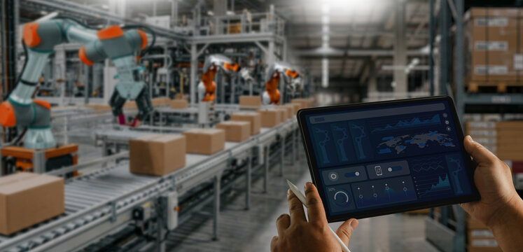 Operator monitoring automated warehouse operations on a tablet with robotic systems and conveyor lines handling packages, representing smart warehouse management, logistics automation, inventory contr