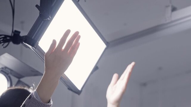 Low Angle View of Female Lighting Technician Checking Brightness of LED Panel Light with Hands
