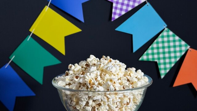 A bowl of popcorn on the table and colorful flags in the background. Decoration for a Brazilian June festival. Arrai&aacute;.