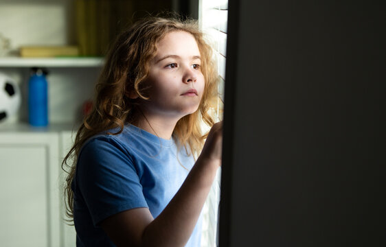 Cute teen child in window light. Kid looking outside with hopeful. Kid watching light through blinds with hope. Kids hopeful mood. Child waiting by the window with hope. Hopeful child concept.