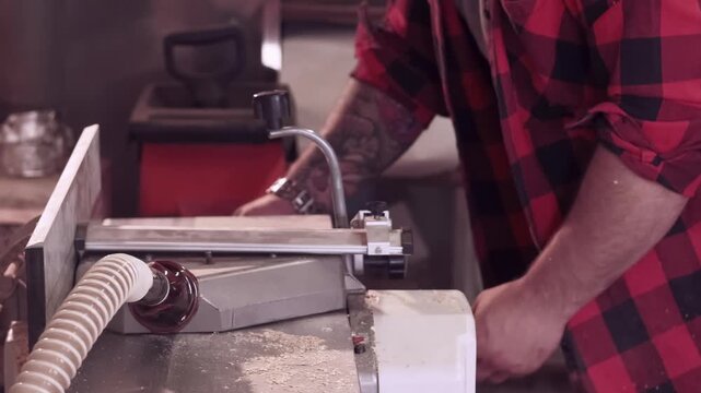 Joinery occupation. Furniture making. Jointer hand processing wood on professional thickness planer with dust collection hose equipment.