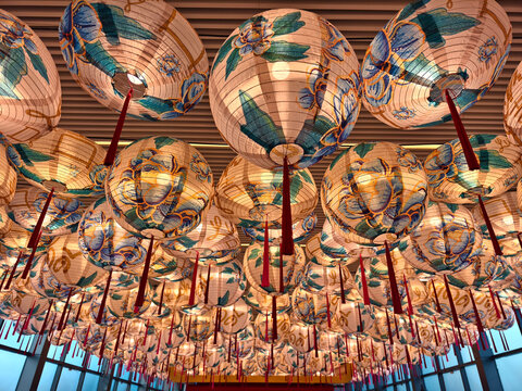 Gold lanterns fill ornate temple ceiling, warm glow casting patterned shadows, red tassels swinging