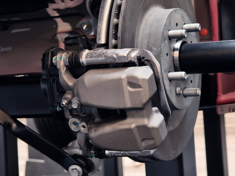 Closeup brake caliper and rotor detail, piston housing, brake pad edges, hydraulic line, metal.