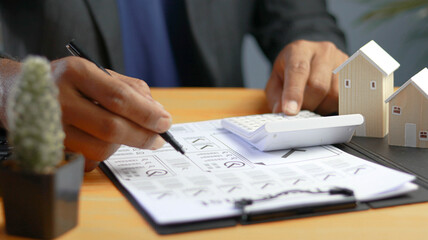 Real estate investor reviewing property valuation documents with calculator and house models on...