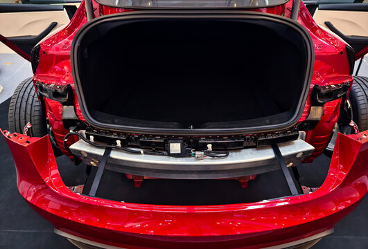 Red car rear bumper open trunk reveals exposed crash beam, mounting brackets, sensors, inner chassis.