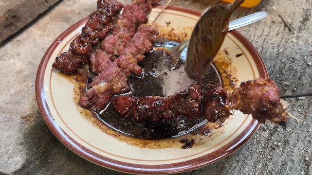 close up view of goat satay being coated with spices on the plate. skewers. eid al adha. idul adha. sate kambing, sapi. indonesian food or culinary. side, front. top, high angle, above. 