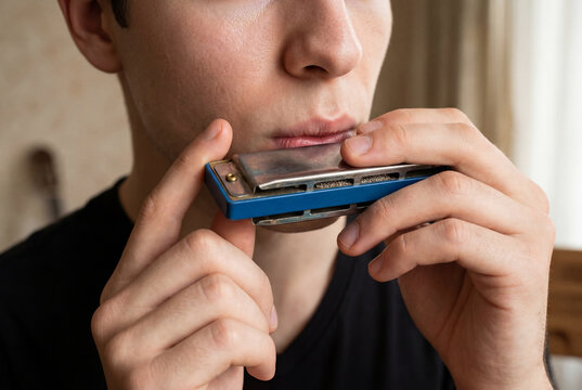 Close up of a person playing a blues harmonica with hands near the mouth