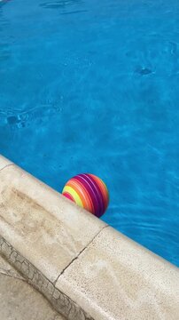 Colorful striped beach ball floating at the edge of a swimming pool