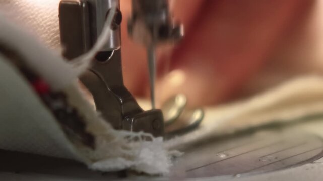 Seam textile. Garment making. Woman hand stitching parts of white linen edge with sticking treads on professional tailor electrical equipment.