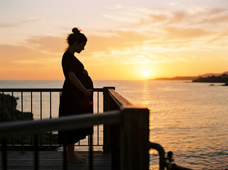 Fototapeta premium Pregnant woman silhouette on balcony overlooking ocean at sunset image