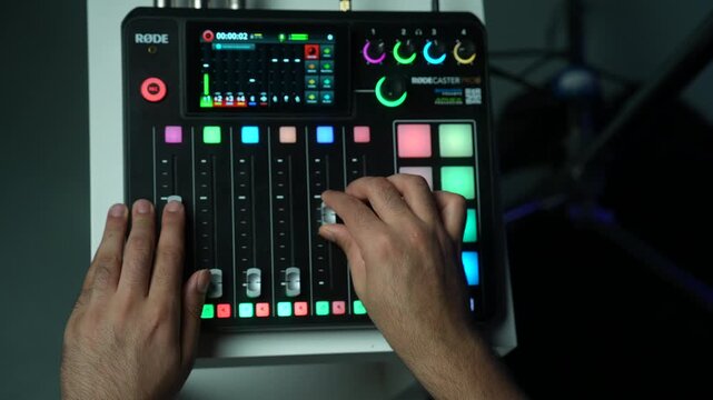 Close up of a sound engineer hand adjusting dials and pressing buttons on a professional audio mixing console console desk with colorful LED lights in a podcast studio