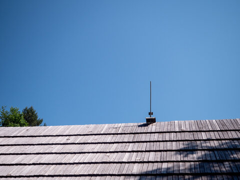 Lightning rod installed on a traditional wooden shingle roof under a clear blue sky. Roof protection system designed to reduce lightning strike and fire risks.