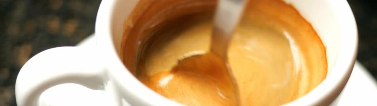 Espresso with golden crema in a white ceramic cup spoon stirring rich foamy dark brew morning caffeine ritual close up indoors.