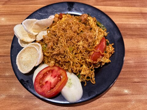 Close up of authentic Indonesian mie goreng, fried noodles dish topped with meat floss, crackers, and sliced tomato.
