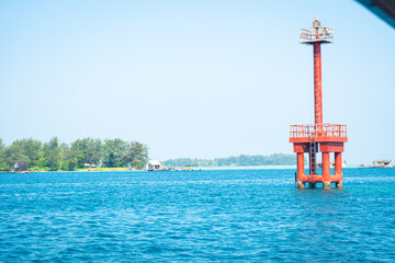 Obraz premium Red navigational buoy tower in calm coastal waters with distant shoreline and greenery