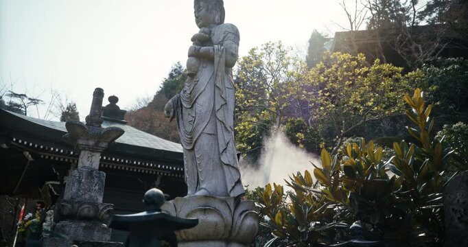 Old Kannon Stone Statue at Japanese Temple with Incense Smoke - Steady Cam
