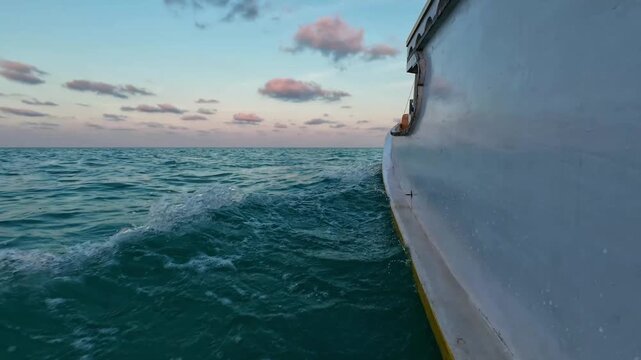 Low angle side view of a wooden boat cruising through open sea at sunset