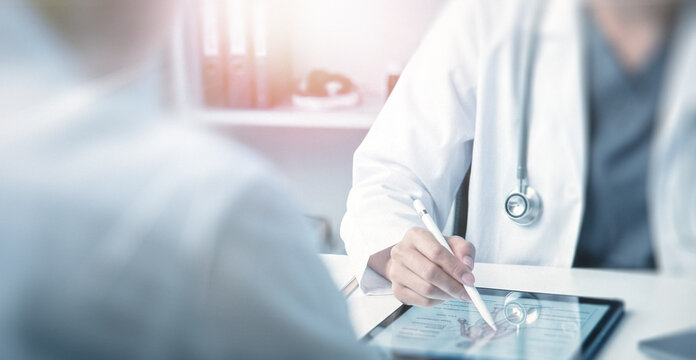 A healthcare professional in a white coat using a tablet to explain something to a patient, highlighting the importance of technology in modern medicine.
