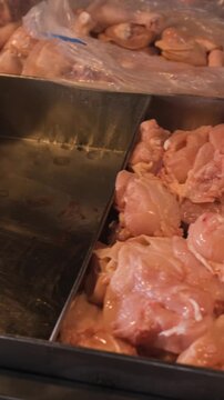 Vertical video. Market meat stall in Thailand displaying chopped chicken pieces, giblets and whole bird carcasses arranged together on a counter for sale. Poultry market concept