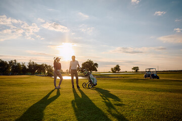 Naklejka premium Full length of happy golfers communicating on golf course at sunset.