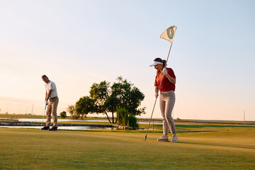 Obraz premium Couple of golfers enjoying a round of golf at sunset.