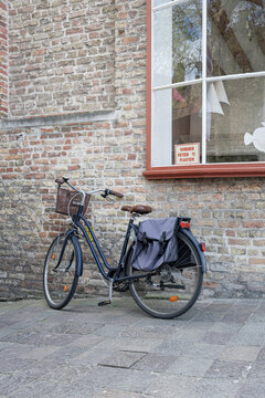 Classic blue city bicycle parked on a cobblestone pavement against an old brick wall with a large window and a no bicycle parking sign.
