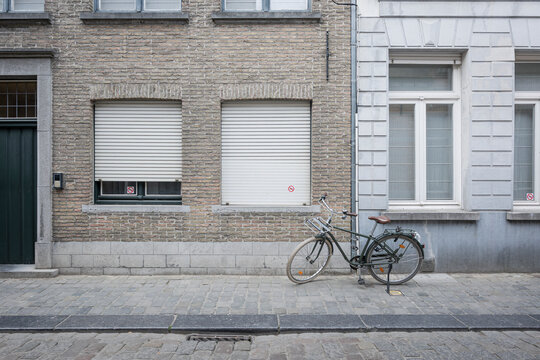 Classic green commuter bicycle parked on a cobblestone sidewalk between two different building facades with windows, roller shutters, and a no bicycle parking sticker.