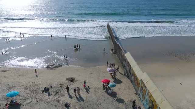 Aerial High Angle Tracking of Border Wall Fence Cutting Into Pacific Ocean Waves in Tijuana Mexico.