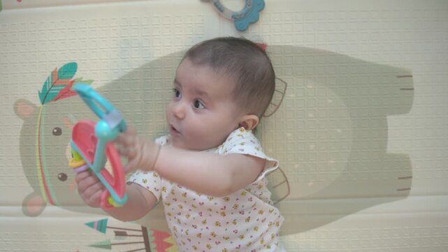 Overhead close-up of a baby holding a colorful toy on a soft play mat at home, ideal for parenting, infant development and playful childcare themes.