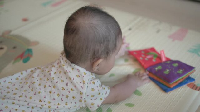 Baby lying on a soft play mat at home during tummy time, reaching toward a colorful fabric book for early learning, sensory play and infant development themes.