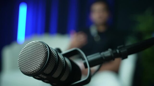 Speaker talks on sofa behind close-up microphone in modern recording studio setup