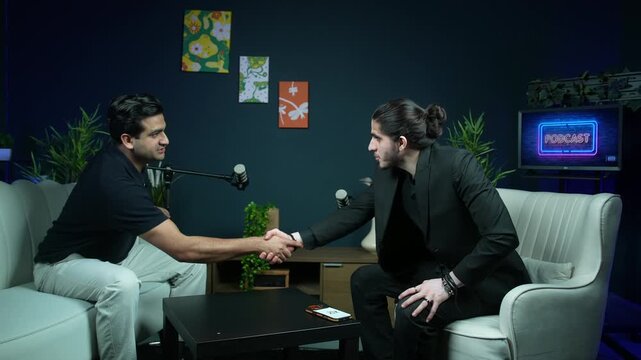 Two men finishing a podcast discussion and shaking hands in a modern studio setting