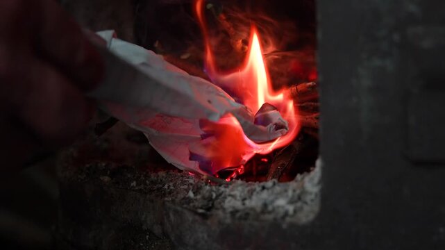 Hand lighting fire with paper in wood stove close up