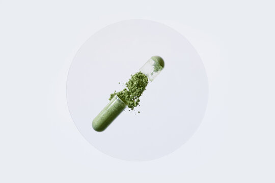 Open transparent capsule spilling green powder on white surface