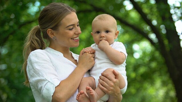 Happy mother holding baby outdoors in park, smiling woman with newborn son in nature, family love concept