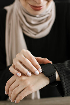 A woman wearing a hijab and a black top checks her modern smartwatch on her wrist