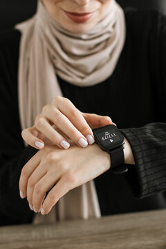 A woman wearing a hijab and a black top checks her smartwatch displaying health data