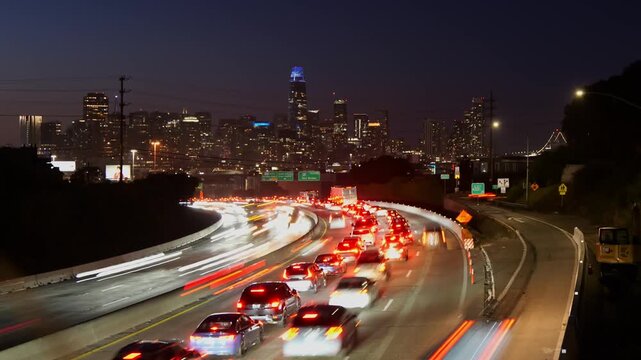 Long exposure view of cars creating light trails on a busy highway at night, with the illuminated San Francisco skyline, including the Salesforce Tower and Bay Bridge, in the background