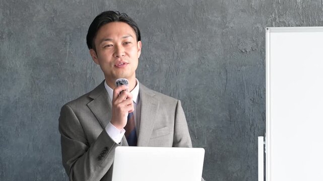 グレー背景でプレゼンをするスーツを着た日本人男性