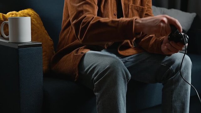 A male gamer in his twenties is playing a video game while sitting comfortably on a couch. He holds a game controller and enjoys the immersive experience in a cozy indoor setting