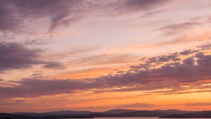 Fototapeta premium Vibrant Sunset Sky Over Calm Water and Distant Mountains.