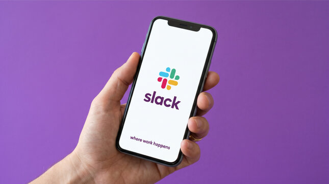 Hand holding a smartphone with the Slack messaging application splash screen logo on the display. Professional communication and collaboration software for teams. Background in purple brand color.
